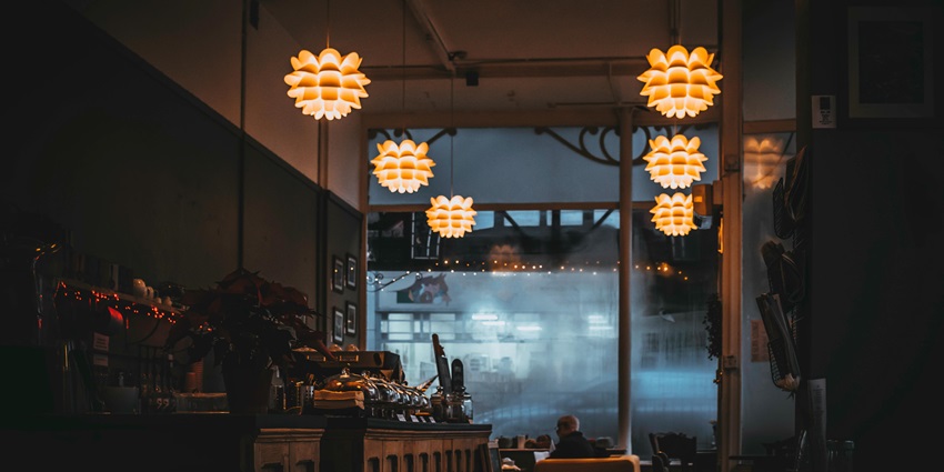 Interior of a cafe with multiple unique hanging lights, an open door, chairs and tables